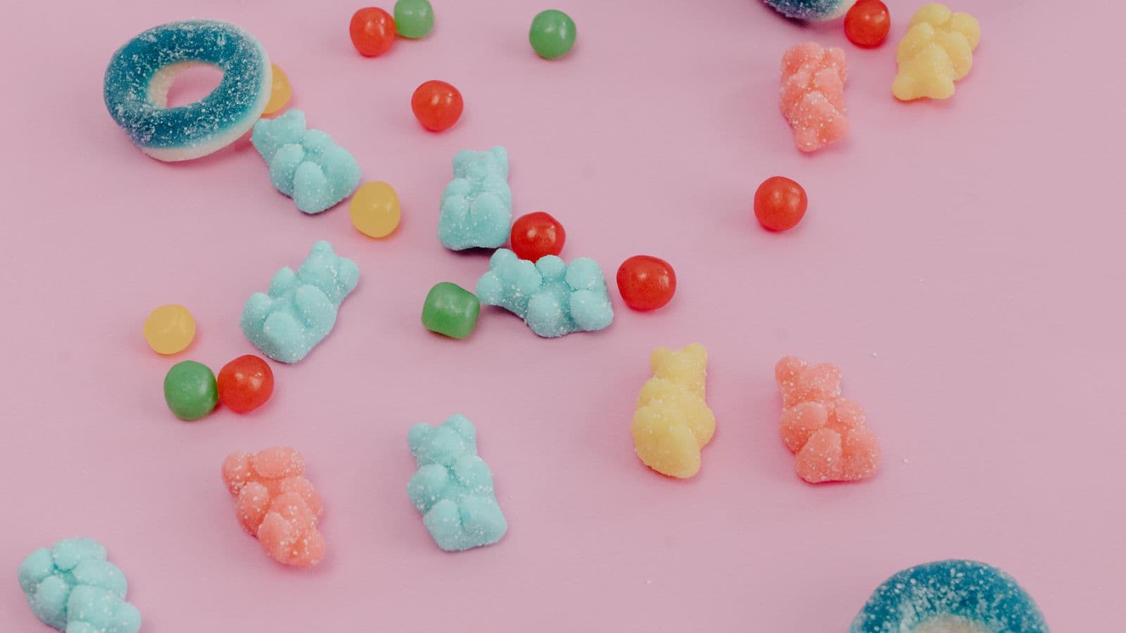 Colorful gummy candies scattered on a pink surface next to a weekly pill organizer.